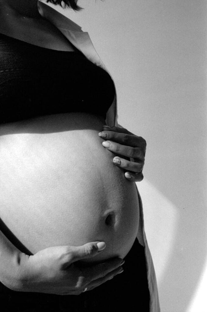 Black and white photo of a pregnant woman gently holding her belly.